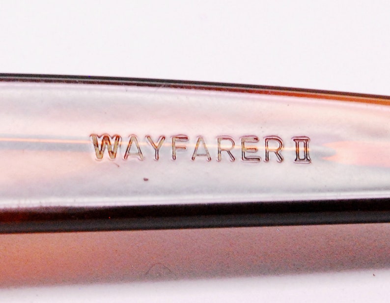 Puede incluir: Primer plano de la inscripci&oacute;n "WAYFARER II" en un marco de pl&aacute;stico marr&oacute;n.