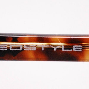 May include: Close-up of the brown tortoiseshell temple arm of a pair of spectacles. The arm is engraved with the text "NEO STYLE DESIGN".