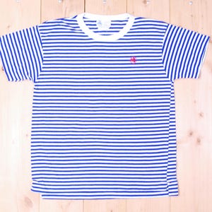 以下が含まれることがあります： 白と青のストライプのTシャツで、前面に小さな赤い刺繍のロゴが付いています。