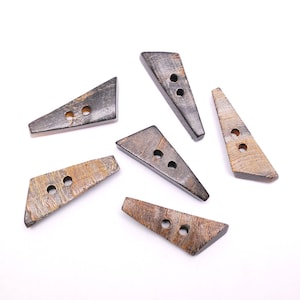 May include: Six triangular buttons with two holes each, in a variety of natural tones including dark brown, grey, and tan. The buttons have a textured finish and are arranged on a white background. Each button is approximately 3 cm long.