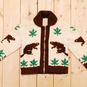May include: A brown and white knit cardigan with a zipper closure. The cardigan features a brown bear and maple leaf pattern.