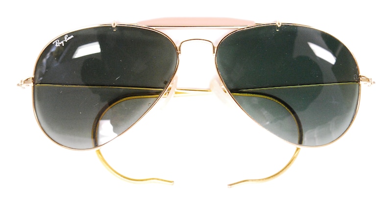 Pode incluir: &Oacute;culos de sol aviador dourados com lentes verdes e um logotipo Ray-Ban na lente esquerda.