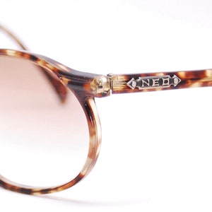 May include: Tortoiseshell eyeglasses with brown tinted lenses. The frame has a silver accent with the word "NEO" on the right temple.