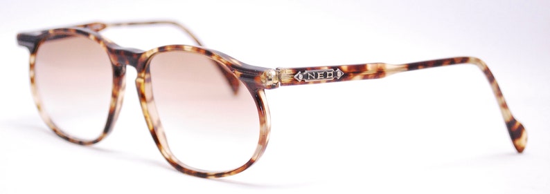 May include: Tortoiseshell eyeglasses with brown tinted lenses. The frame has a silver accent with the word "NEO" on the right temple.