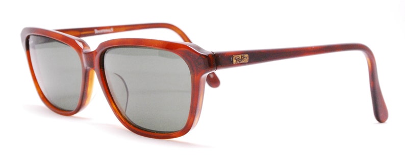 May include: Brown tortoise shell frame sunglasses with green lenses and gold Ray-Ban branding on the right temple.