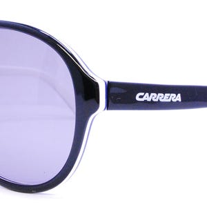 Puede incluir: Gafas de sol aviador negras con una franja blanca en el marco y la palabra "CARRERA" impresa en el lateral.