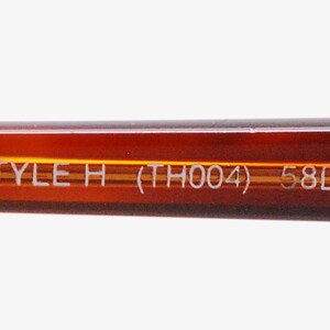 May include: Close-up of the brown plastic arm of a pair of glasses with the text "STYLE H (TH004) 58□14" printed in white.