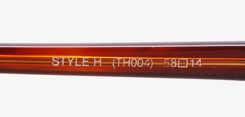 May include: Close-up of the brown plastic arm of a pair of glasses with the text "STYLE H (TH004) 58□14" printed in white.
