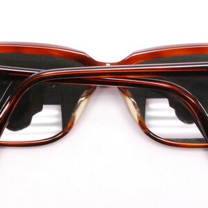 May include: A pair of brown tortoise shell frame sunglasses with dark lenses. The sunglasses have a gold Ray-Ban logo on the right temple.