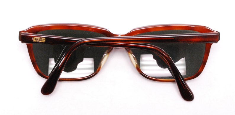 May include: A pair of brown tortoise shell frame sunglasses with dark lenses. The sunglasses have a gold Ray-Ban logo on the right temple.