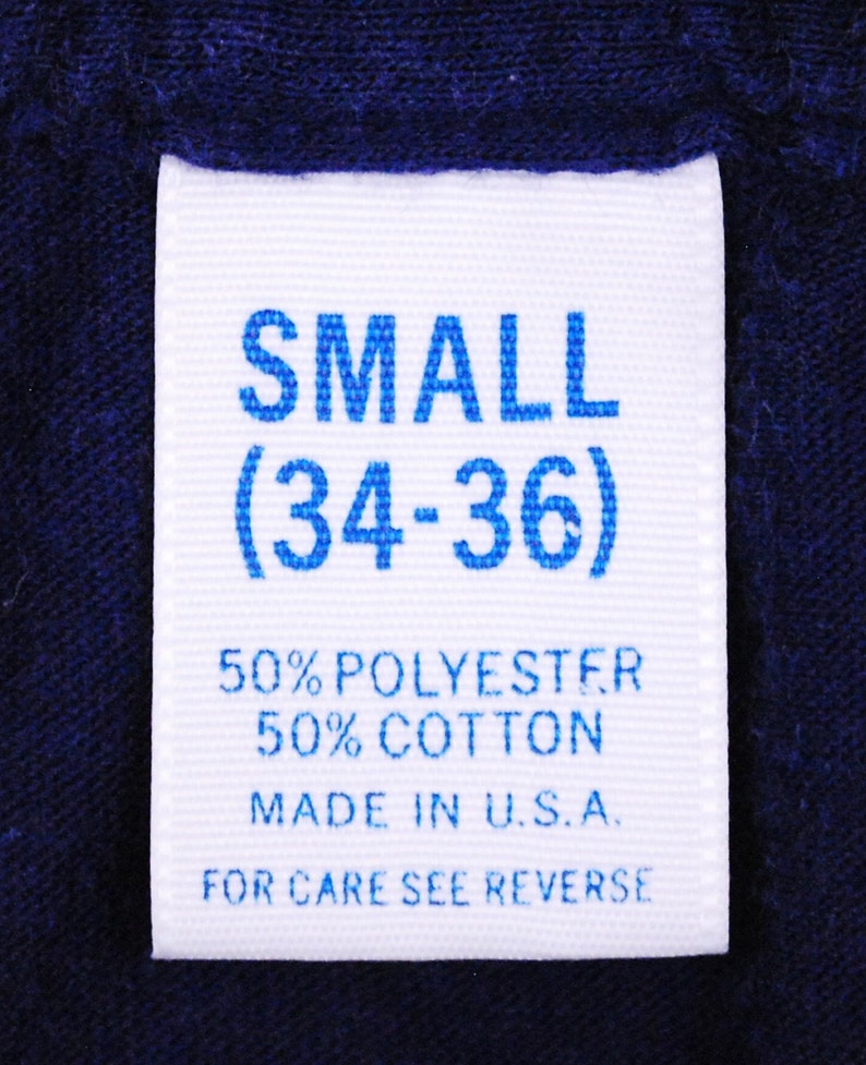 Puede incluir: Etiqueta blanca con texto azul que indica una talla "SMALL (34-36)". La etiqueta tambi&eacute;n dice "50% POLYESTER 50% COTTON MADE IN U.S.A. FOR CARE SEE REVERSE."