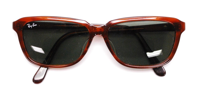 May include: Brown plastic framed sunglasses with dark green lenses. The sunglasses have the Ray-Ban logo on the left frame.