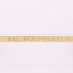 May include: Close-up of the inscription on a pair of gold-tone Ray-Ban sunglasses. The inscription reads "B&L RAY-BAN U.S.A."