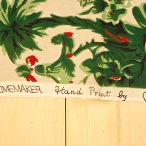 May include: A beige fabric with a green and red floral pattern. The fabric has the text "a HOMEMAKER Hand Print by HEES" printed on the bottom.