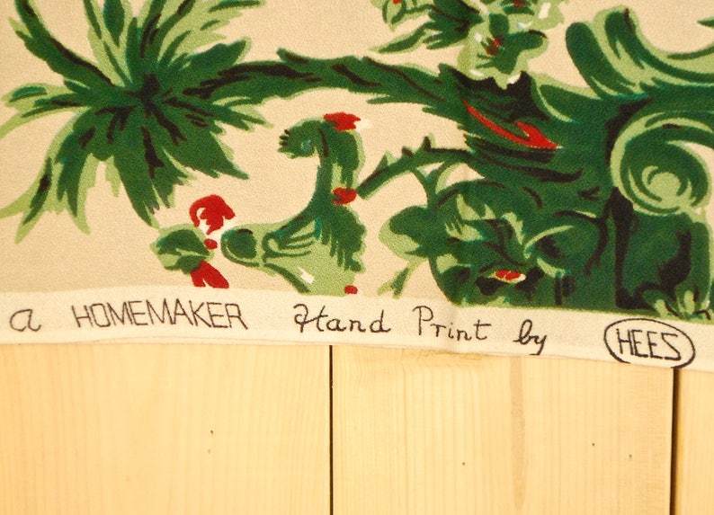 May include: A beige fabric with a green and red floral pattern. The fabric has the text "a HOMEMAKER Hand Print by HEES" printed on the bottom.