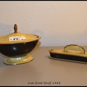 May include: A vintage two-piece set of black and cream colored ceramic containers. The larger container has a lid with a wooden knob and a price tag that reads "$5 - Set". The smaller container has a handle and is rectangular.