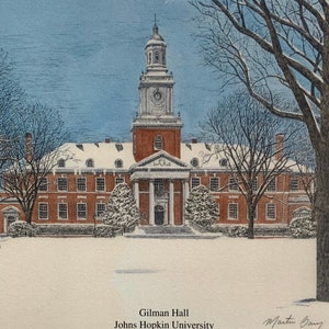 May include: A winter scene of Gilman Hall at Johns Hopkins University. The building is brick with white trim and a tall clock tower. The trees are bare and covered in snow. The ground is also covered in snow. The text "Gilman Hall" and "Johns Hopkins University" is printed below the image.