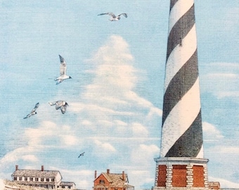 May include: A black and white striped lighthouse stands tall against a blue sky with white clouds.  There are several seagulls flying in the sky.  Two small houses are in the foreground with a sandy beach and grass.