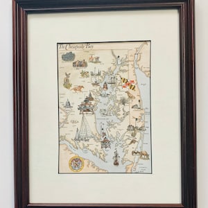 May include: A framed illustration of the Chesapeake Bay, Maryland, with a detailed map of the bay and surrounding areas. The illustration features various landmarks, including lighthouses, ships, and buildings. The title "The Chesapeake Bay" is printed at the top of the map.