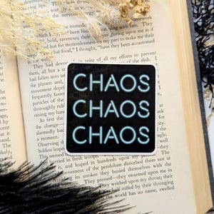May include: A black sticker with the word "CHAOS" repeated three times in a neon blue font. The sticker is placed on a book with text about rats.