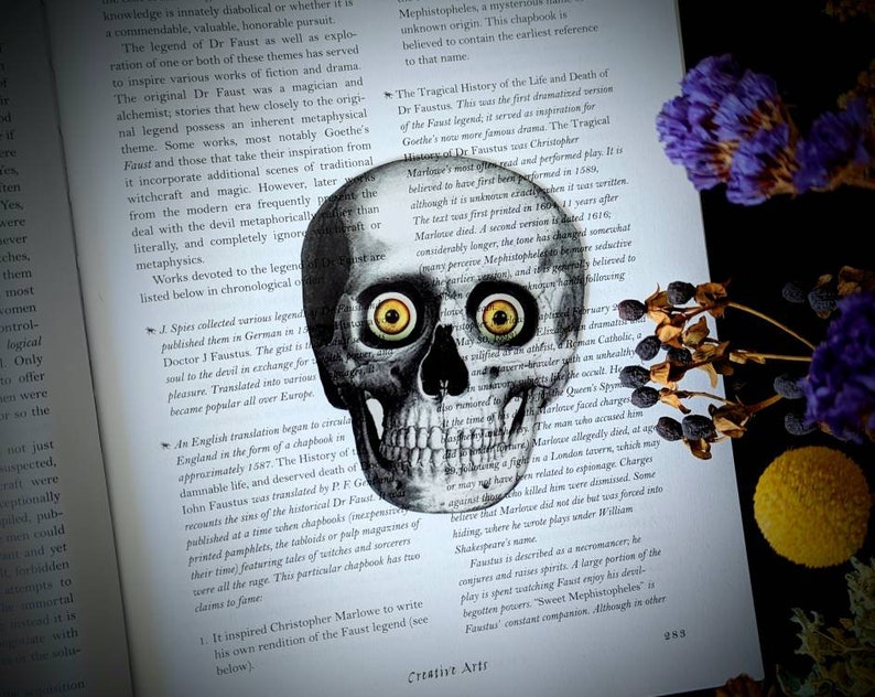 May include: A black and white illustration of a human skull with large, bright yellow eyes. The skull is superimposed on a page of text about the legend of Dr. Faustus. The text discusses the history of the legend and its various interpretations.