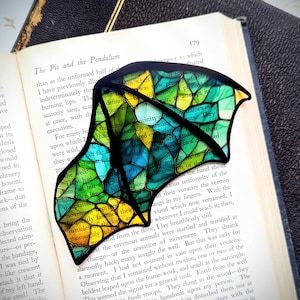 May include: A stained glass bookmark with a colorful, abstract design. The bookmark is shaped like a wing and features shades of green, blue, yellow, and orange.