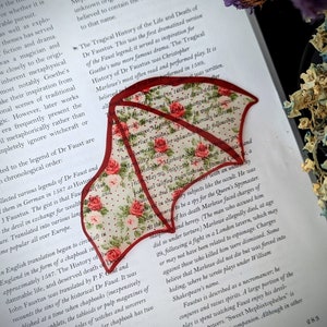 May include: A red and white floral bookmark with a red border. The bookmark is shaped like a wing and has the text "The Tragical History of the Life and Death of Dr Faustus" printed on it.