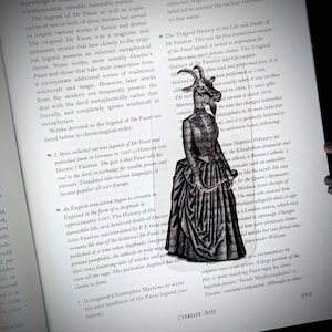 May include: A black and white illustration of a woman in a long dress with a goat head. The woman is holding a string of pearls in her right hand. The illustration is from a book about the legend of Dr. Faustus.