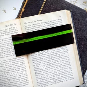 May include: A close-up of a page from a vintage book titled "The Pit and the Pendulum" by Edgar Allan Poe. The text describes a scene where the narrator is being tormented by rats. The page is highlighted with a green sticky note.