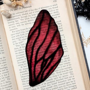 May include: A close-up of a red and black stained glass bookmark with a swirling design. The bookmark is resting on a page of an open book with the text "Pit and the Pendulum" visible.