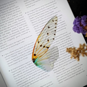 May include: A close-up of a book with a colorful butterfly bookmark. The book is open to a page about the legend of Dr. Faustus. The butterfly bookmark has orange, yellow, blue, and green wings.
