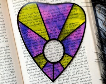 Può includere: Un segnalibro a forma di cuore in vetro colorato con un design viola, giallo e rosa. Il segnalibro presenta una citazione dal libro "Il pozzo e il pendolo" di Edgar Allan Poe: "Avevano divorato, nonostante tutti i miei sforzi per impedirlo, tutto tranne un piccolo resto del contenuto del piatto."