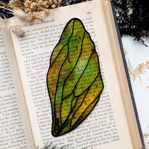 May include: A stained glass butterfly bookmark with a yellow, green, and black design. The bookmark is placed on an open book with text about rats.