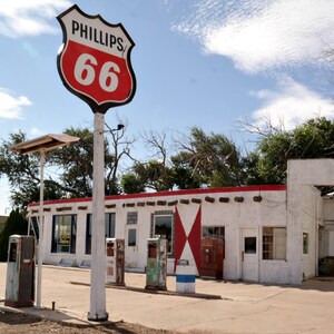 Puede incluir: Una gasolinera vintage con un letrero de Phillips 66 rojo y blanco. El edificio es blanco con molduras rojas y tiene un letrero de la Ruta 66 descolorido en el lateral. Hay surtidores de gasolina y un letrero de Phillips 66.