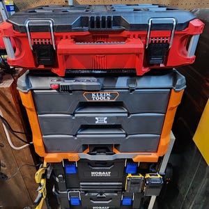 May include: A stack of three toolboxes. The top toolbox is red and black with the brand name "Klein Tools" on the side. The middle toolbox is orange and black with three drawers and the text "Mod Box" on the front. The bottom toolbox is black with the brand name "Kobalt CaseStack" on the front.