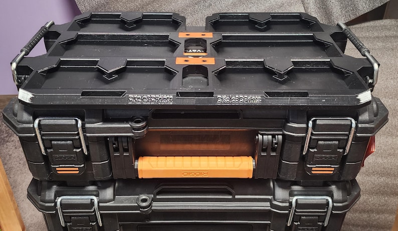 May include: Two black and orange toolboxes stacked on top of each other. The toolboxes have metal latches, handles, and orange accents. The top of the toolbox has a textured design. The text "CKC3DPrint" is visible on the side of the toolbox.