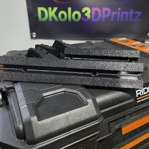 May include: Black 3D-printed components stacked on a black Ridgid Pro Gear System Gen 2.0 case. The components have a textured surface. A banner in the background reads "DKolo3DPrintz" in green, purple, and yellow.