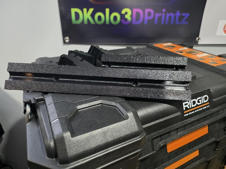 May include: Black 3D-printed components stacked on a black Ridgid Pro Gear System Gen 2.0 case. The components have a textured surface. A banner in the background reads "DKolo3DPrintz" in green, purple, and yellow.