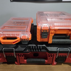 May include: Stack of three toolboxes in orange, red, and black. The top two boxes are orange with clear lids and black latches. The bottom box is red with black accents and a black handle. The toolboxes are designed for storage and organization.