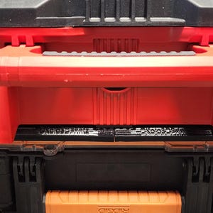 May include: A red and black tool box with a handle and multiple latches. The tool box has a black top and bottom section with a red center section. The latches are black and the handle is red.