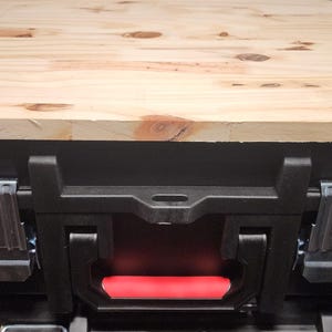 May include: A black toolbox with a light-colored wooden top. The toolbox has two clear plastic latches and a red handle. The wooden top is rectangular with a beveled edge.