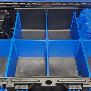 May include: Open black storage case with blue dividers. The case contains a black device on the left and a blue device on the right. The dividers create multiple compartments within the case, offering organized storage.