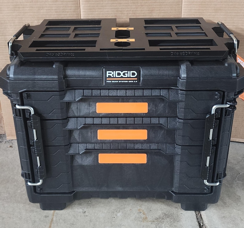 May include: Black RIDGID Pro Gear System 2.0 tool box with orange accents. The toolbox has a black top tray and metal latches. The text "RIDGID" is visible on the front of the toolbox.