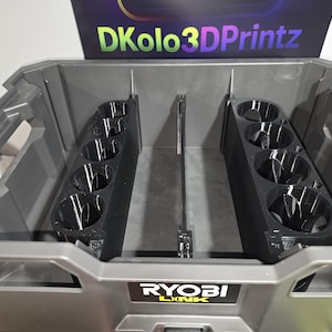 May include: A gray Ryobi Link tool box with black cup holders. The cup holders are designed to fit inside the tool box. The text "DKolo3DPrintz" is visible on the top of the tool box.