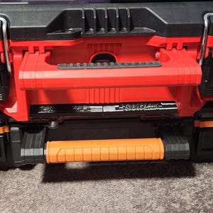 May include: A red and black tool box with a retractable orange handle. The toolbox has black latches and a black top. The toolbox is designed for storing tools and equipment.