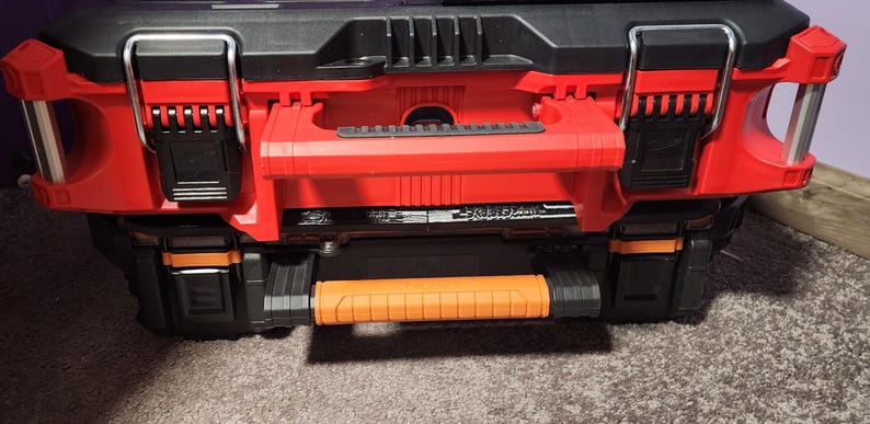 May include: A red and black tool box with a retractable orange handle. The toolbox has black latches and a black top. The toolbox is designed for storing tools and equipment.