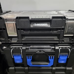 May include: A black Husky brand tool box with a clear top lid and silver metal latches stacked on top of a black tool box featuring a blue handle and blue locking latches. The Husky logo is printed in white on a black rectangular nameplate.
