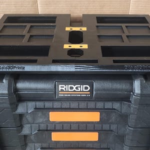 May include: Black RIDGID Pro Gear System Gen 2.0 tool box with a black organizer tray on top. The tray has multiple compartments and the text "Dkolo3Dprintz". The tool box has orange accents and metal latches.