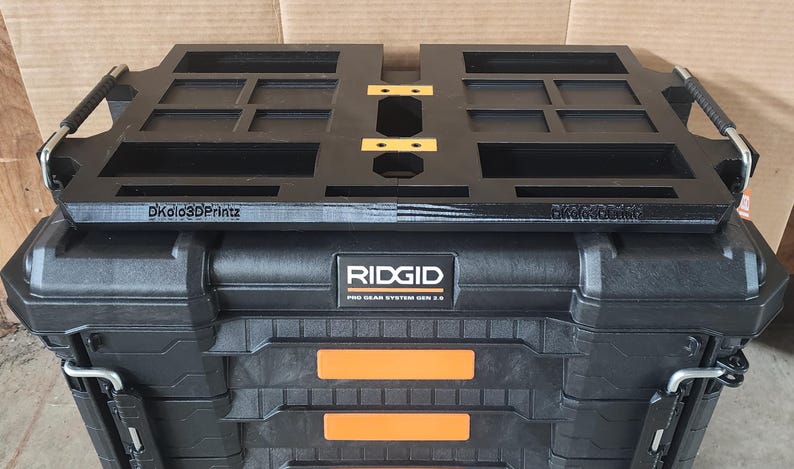 May include: Black RIDGID Pro Gear System Gen 2.0 tool box with a black organizer tray on top. The tray has multiple compartments and the text "Dkolo3Dprintz". The tool box has orange accents and metal latches.