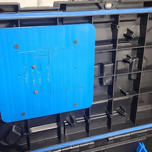 May include: Open black and blue storage case with a blue rectangular insert. The insert has text and is secured with screws. The case has a blue rubber seal around the rim.